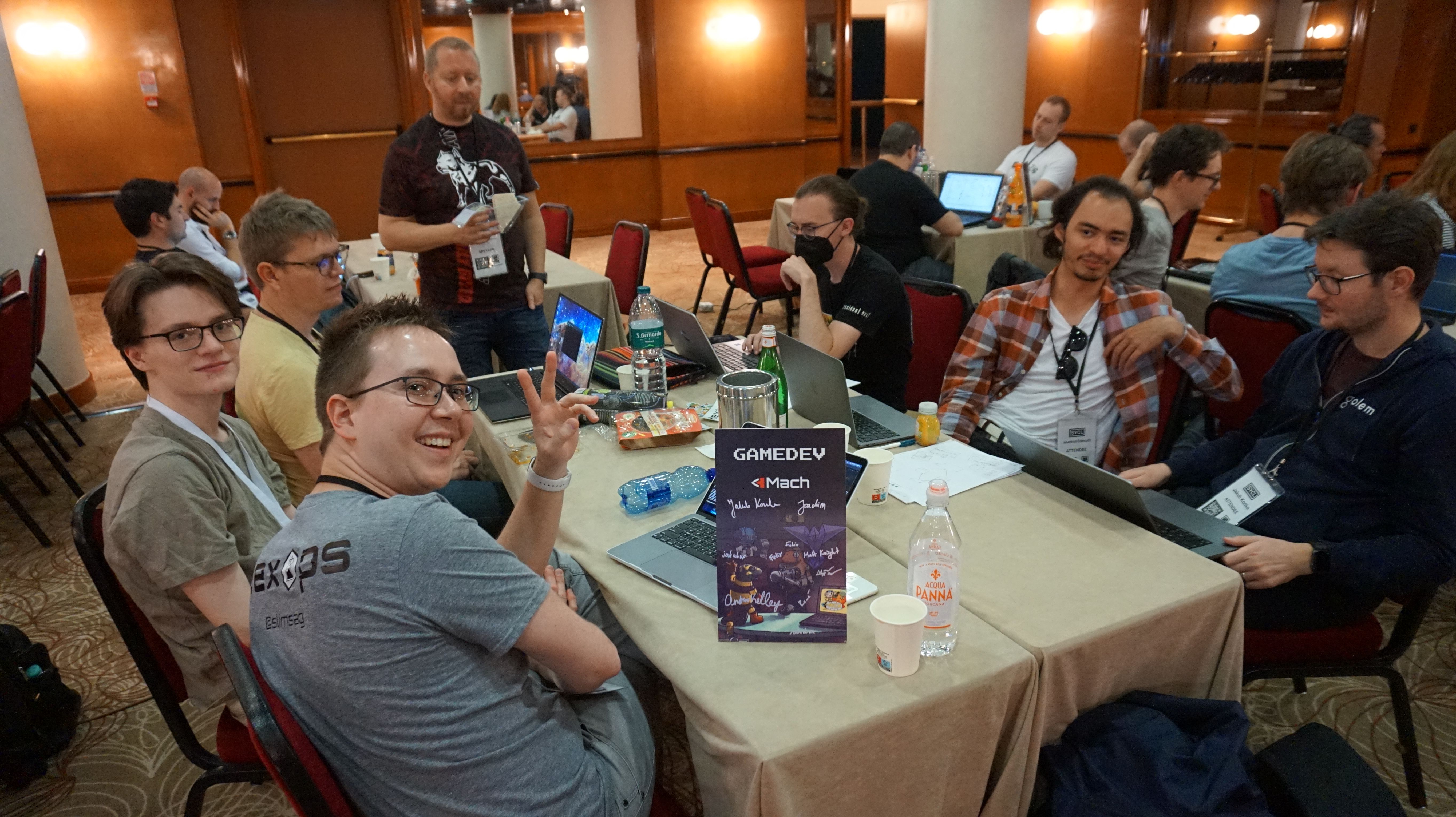 A photo from SYCL 2022 showing a group of people sitting at a table with their laptops open.